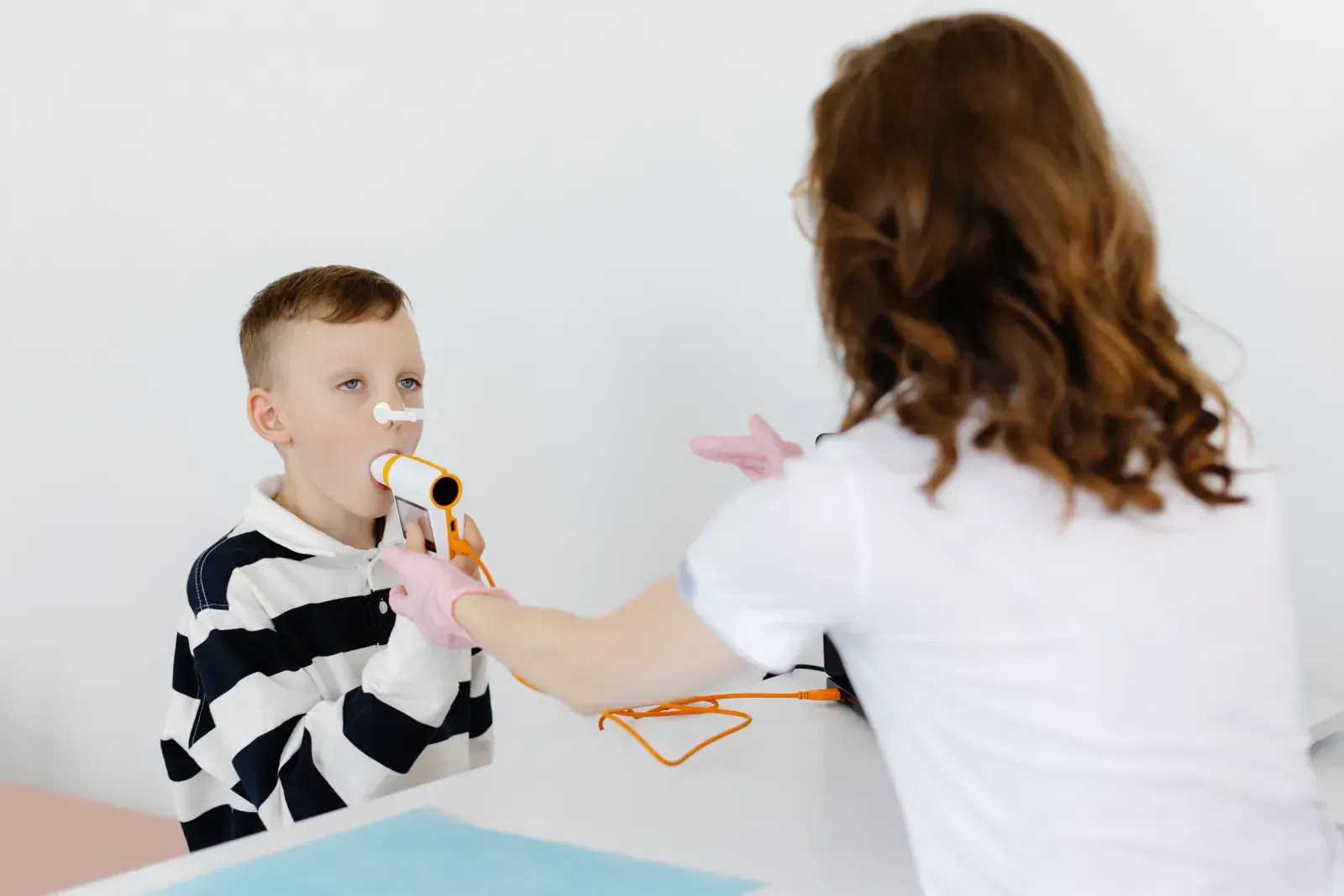 Niño realizando un estudio de espirometría con boquilla y pinza nasal guiado por la doctora