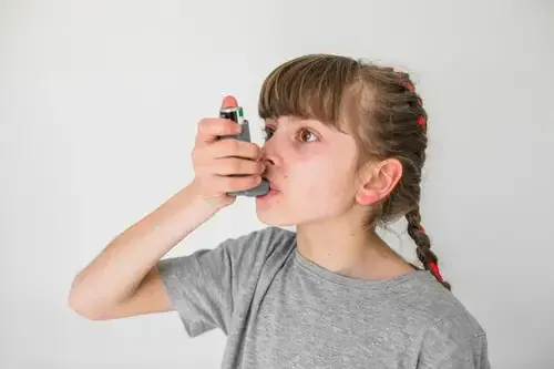 Niña usando su inhalador para controlar el asma infantil