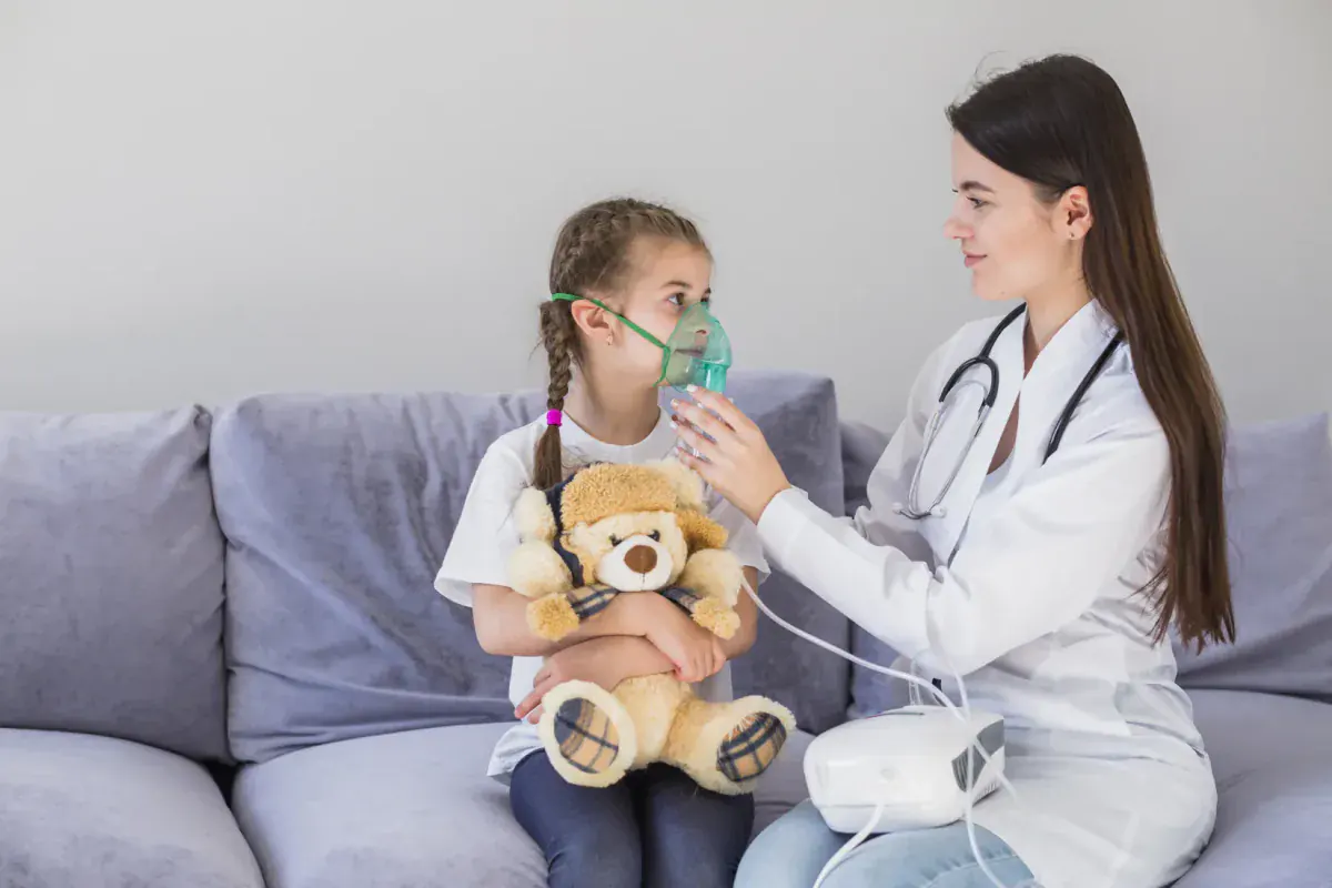 Tratamiento del asma infantil: doctora colocando una mascarilla de nebulización a una niña con su osito